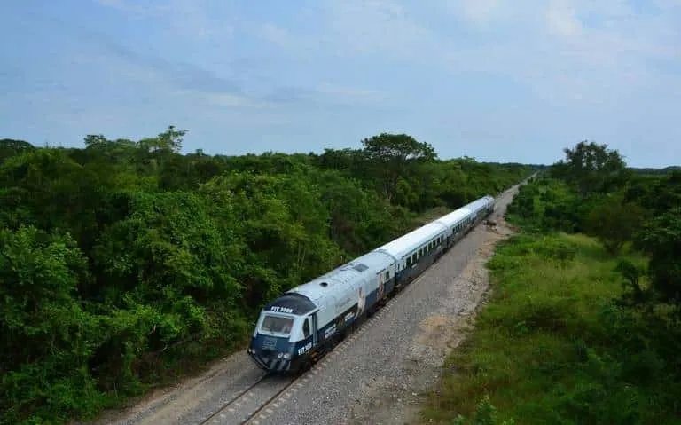 Passenger train on tracks in southern Mexico with station platforms and low hills in the distance