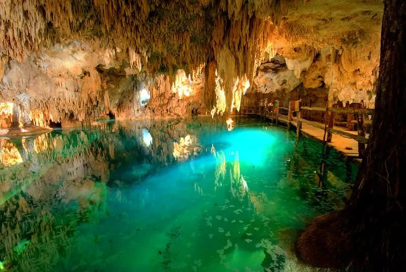 Aktun Chen cenote cave near Tulum — natural and artificial lighting illuminating stalactite formations above a clear pool