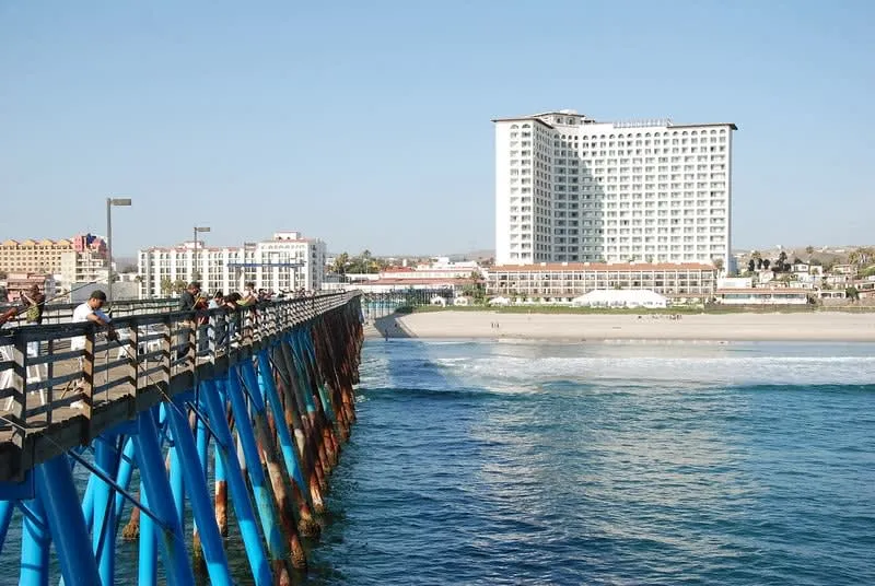 Ocean pier stretching toward waterfront buildings under a clear blue sky