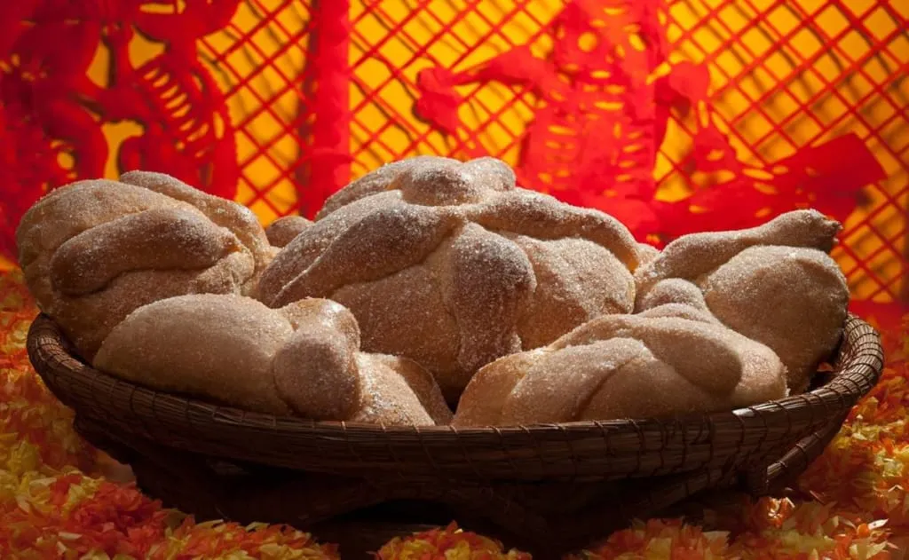 Pan de muerto loaves placed beside candles and marigolds