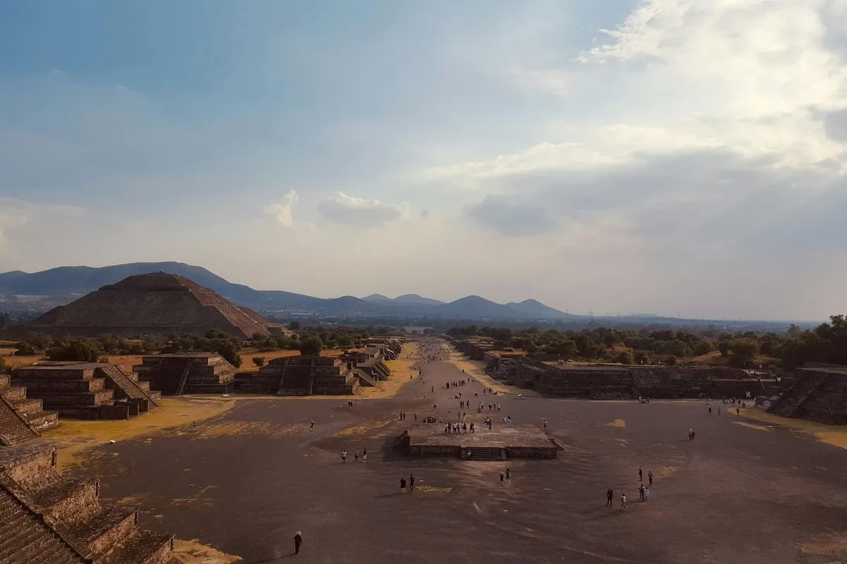 Wide view of a stone archaeological site with pyramids, a central avenue, and scattered people