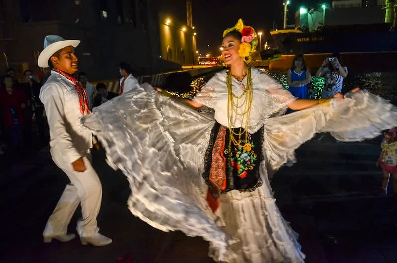 Huapango dancers in white embroidered traditional costume performing zapateado on a wooden tarima platform