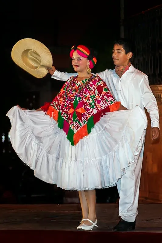 Dance performers wearing white embroidered costumes and wide-brimmed hats