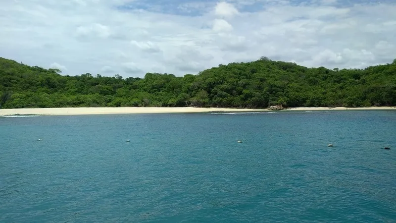 Small tour boat crossing a blue Huatulco bay near rocky headlands