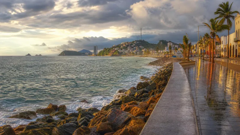 Wide Pacific beach backed by green hills, resort towers, and cloudy summer sky