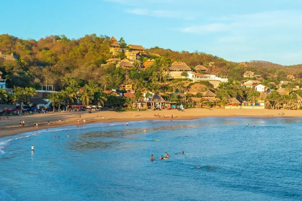 Sandy Mazunte beach with palapas and the Sierra Madre del Sur behind town