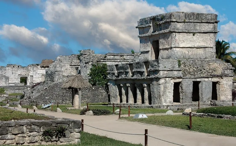 Stone temple and walking paths at the Tulum archaeological site under a cloudy blue sky