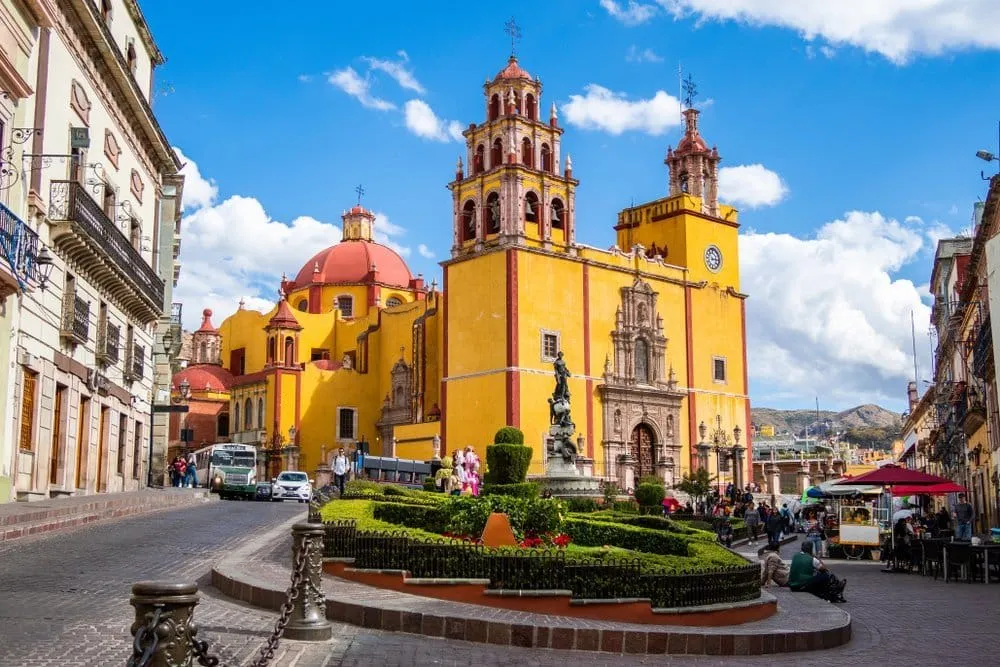 Yellow Guanajuato church beside a garden plaza with pedestrians