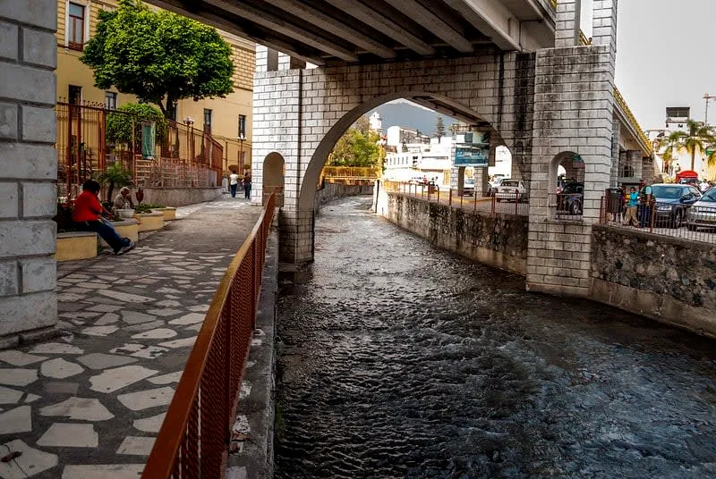 Stone-lined Orizaba river walk with greenery beside the water near the city center