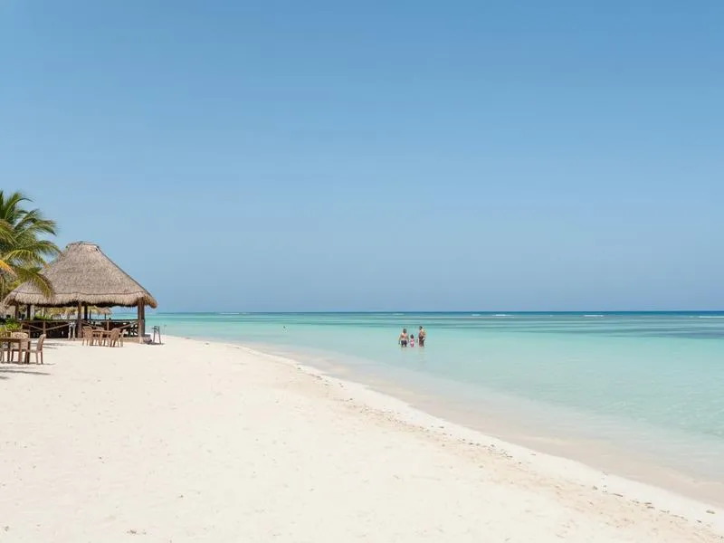 Playa Norte on Isla Mujeres with shallow turquoise water, white sand, palm trees, and palapa tables