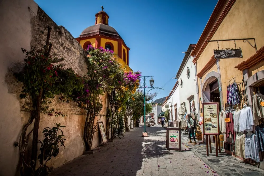Colonial village of Bernal, Querétaro with stone streets and traditional architecture at the base of the Peña de Bernal monolith — small market stalls sell gorditas and artisan crafts