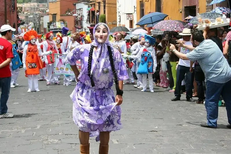 Festival parade through San Miguel de Allende cobblestone streets with traditional costumes and mojigangas giant figures