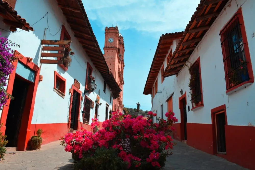 Cobblestone street in Tapalpa Jalisco lined with white-painted colonial buildings and terracotta roof tiles surrounded by pine-forested mountains