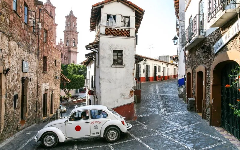 Taxco hillside view in October with green mountains, white houses, and Santa Prisca