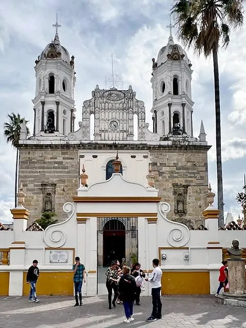Stone church facade in Tlaquepaque framed by a warm May sky