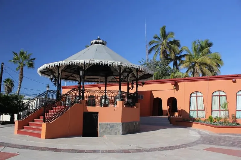 Todos Santos plaza kiosk surrounded by trees, benches, and low buildings in the town center