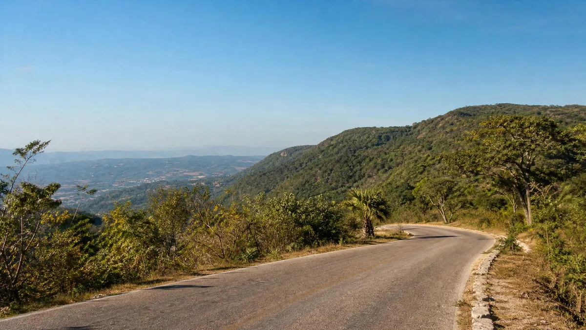 Sunlit road curving through dry green hills in lowland Chiapas