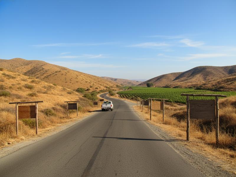 Road from Ensenada into Valle de Guadalupe with dry hills and vineyard signs