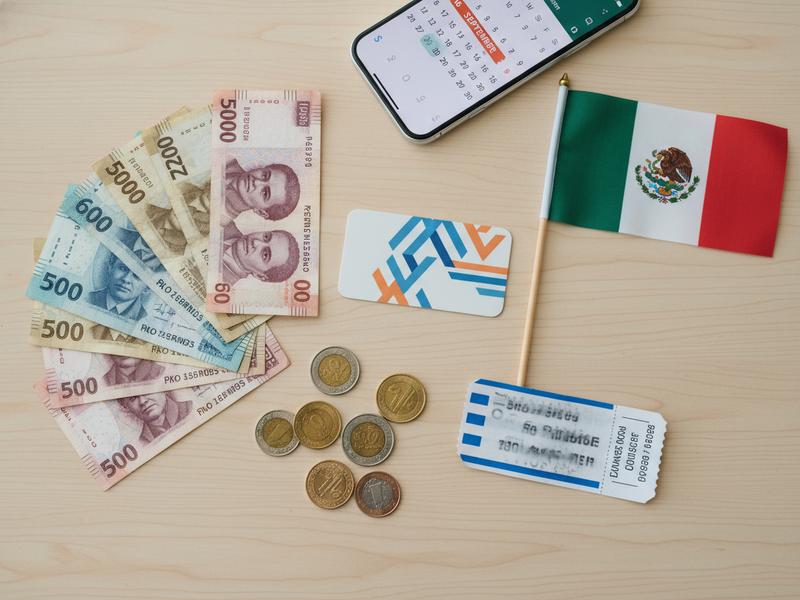 Pesos, a hotel key, a bus ticket, and small tricolor decorations on a table