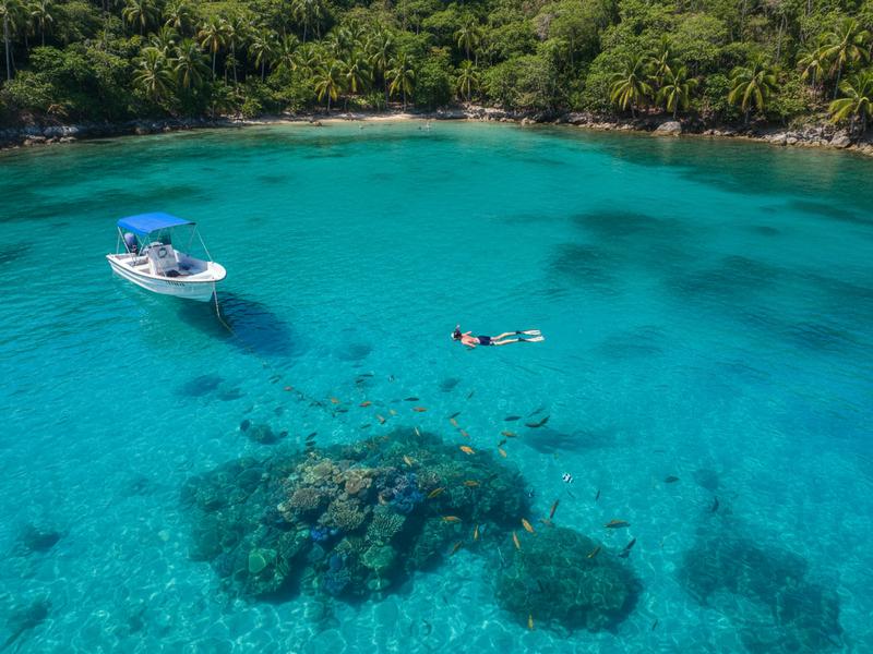 Huatulco bay with crystal clear turquoise water, snorkelers in the water, and lush green hills surrounding the beach