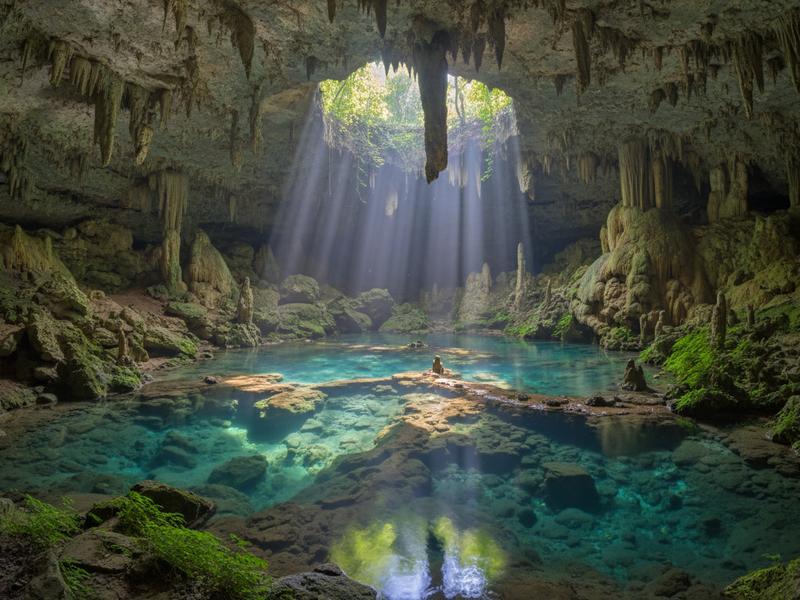 Turquoise pool inside Puente de Dios cave with light streaming through ceiling