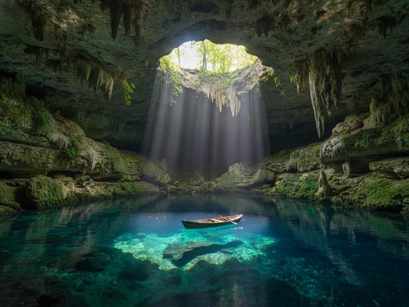 Cenote Ik Kil with hanging vines cascading down the circular opening, swimmers in the turquoise water below