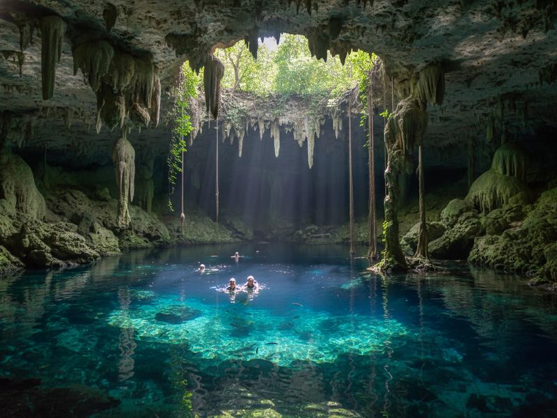 Scuba diver exploring an underwater cave system in a cenote, with light beams penetrating the crystal-clear water