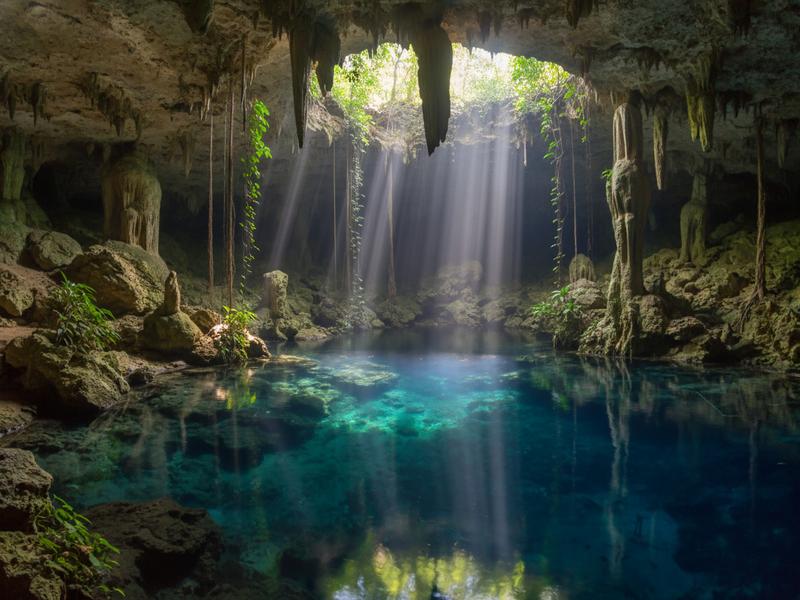 Diver swimming through light beams in crystal-clear cenote water